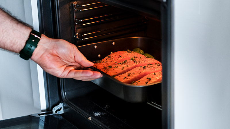 Close-up of hand of man putting raw salmon steak into oven.