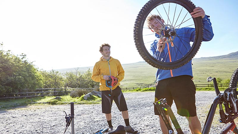 Young male cyclist attaching bicycle wheel to bicycle while another male cyclist watching it. 