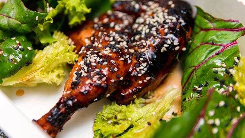 Caramelized BBQ chicken leg quarters with chia seeds sprinkled on top, surrounded with colourful greens.
