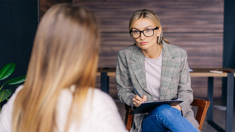 Female psychotherapist jotting down the issues her teenage girl patient experiencing during counselling session.