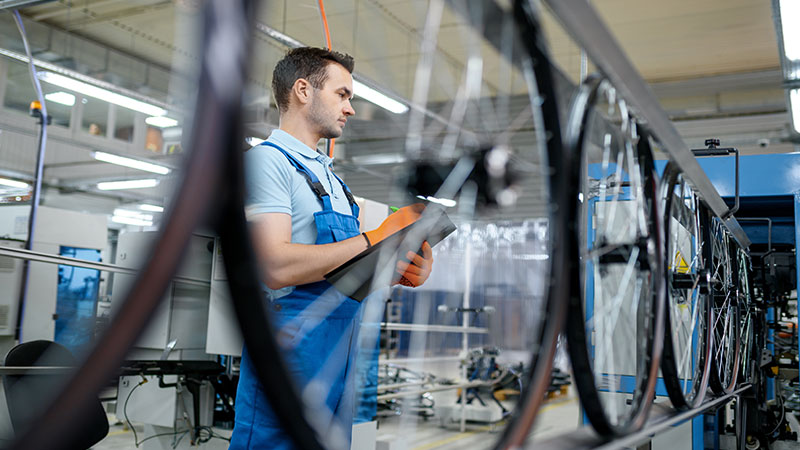 Worker with a notepad in his hand checking bicycle wheels on the assembly line at the factory. 