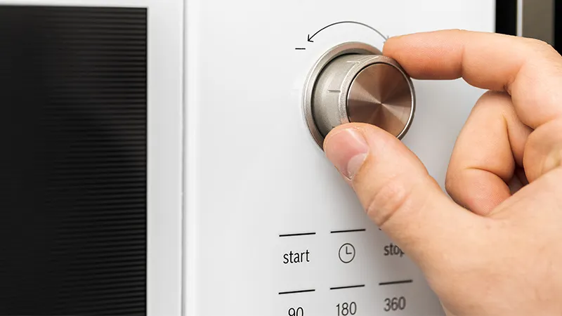 Close-up of hand rotating button of microwave oven for cooking food in kitchen. 
