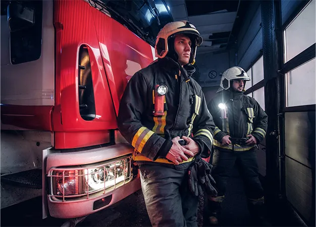Two firefighters stand near the truck at night in a fire depot