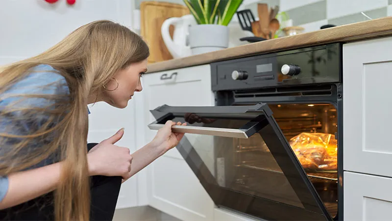 Close-up of young woman putting marinated chicken in baking bag in oven.