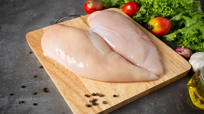 Close-up of raw chicken breasts on wooden cutting board. 