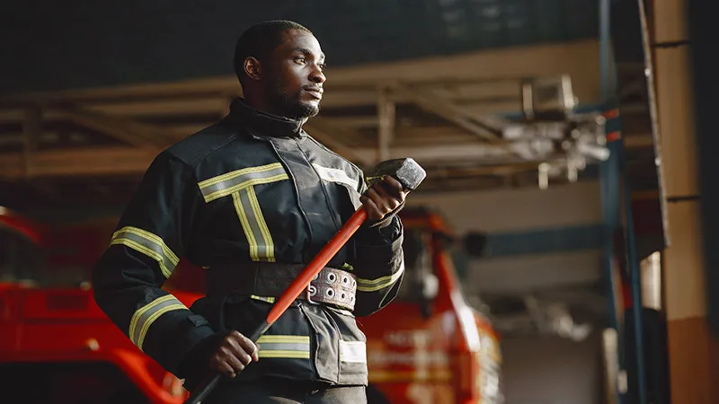 A fireman in uniform prepares for work and holds a hammer in hand