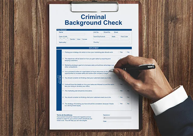 Close-up of man’s hand working on criminal background check form on wooden table.