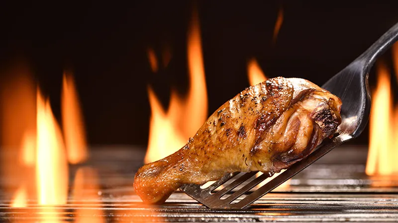 Close-up of grilled chicken leg on the flaming grill.