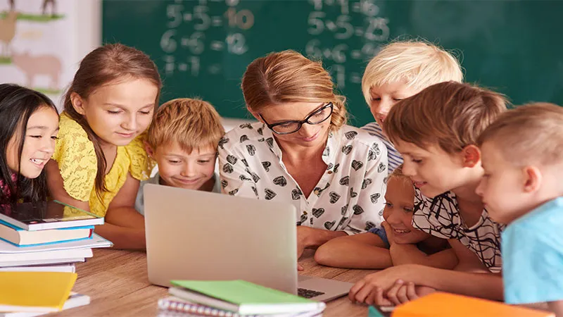 A teacher shows something in laptop in classroom