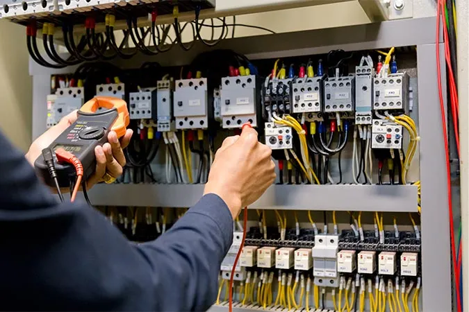 An electrician works in an electrical cabinet by measuring the voltage and current of power lines