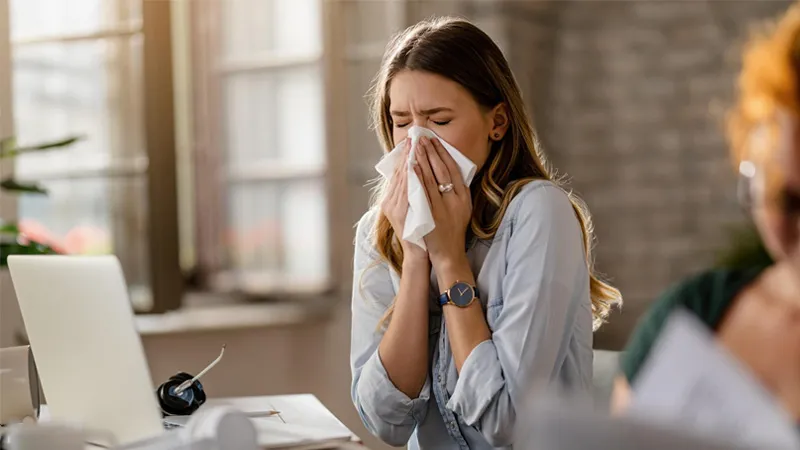 Young female employee sneezing on a tissue while working in the office