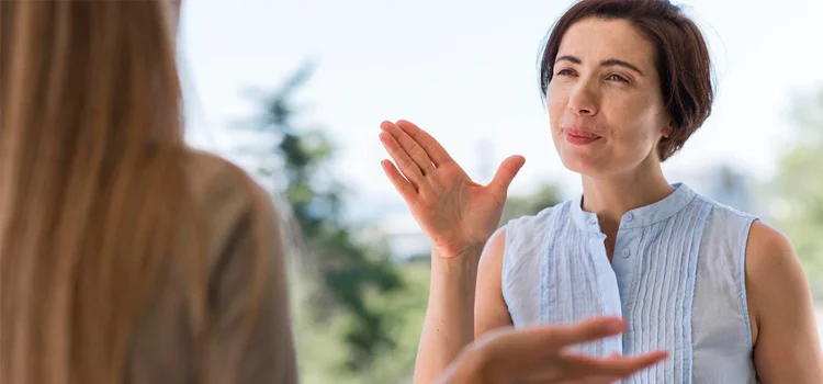 A woman wearing white is communicating through British sign language