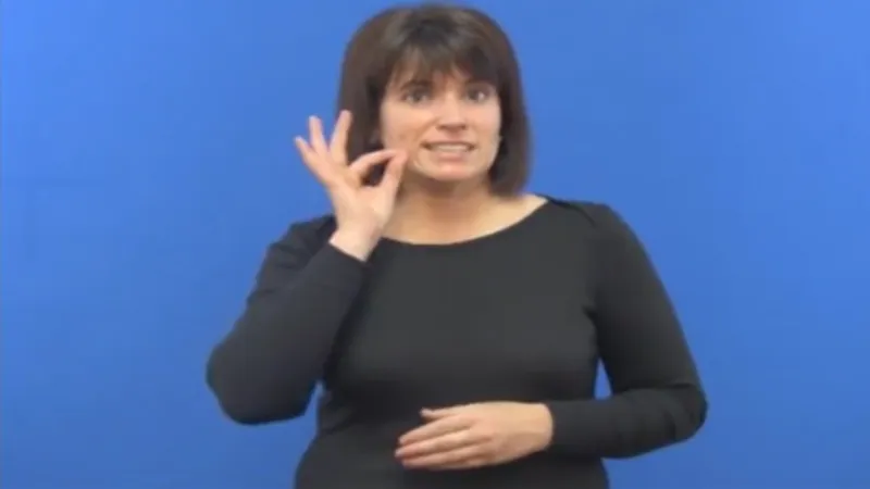 Female tutor teaching how to sign Tea, has her right-hand fingers shaped in the form of O and teeth clenched together