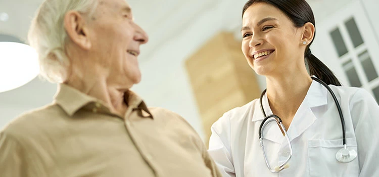 Friendly lady in a white lab coat smiling at a senior citizen in her medical care.
