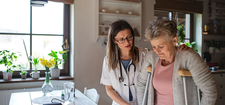 Healthcare worker or caregiver visiting a senior woman indoors at home, helping her to walk.