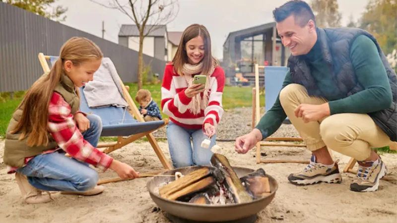 Two girls and man holding marshmallow sticks in a campfire