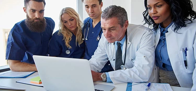 Clinical professionals in a meeting looking something at a computer screen.