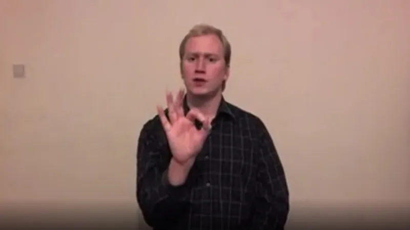 BSL interpreter with one hand raised with thumb touching index finger