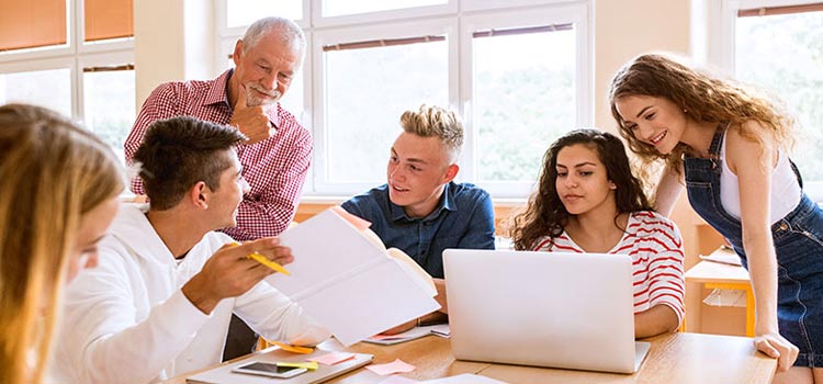 A middle-aged teacher observing a group of college students working on group projects.