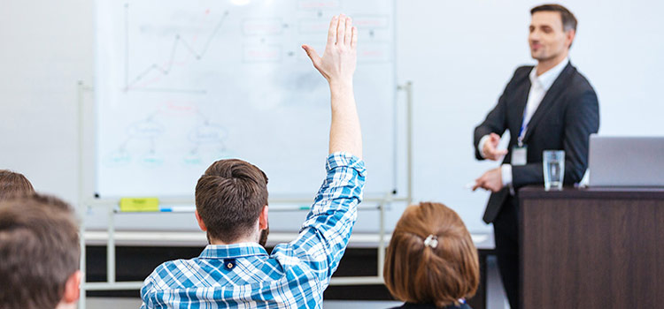 Young teacher conversing with a hand-raised male college student in the classroom.