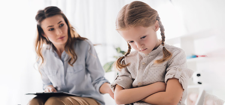 Child psychologist talking to a depressed little girl with crossed arms during therapy session. 