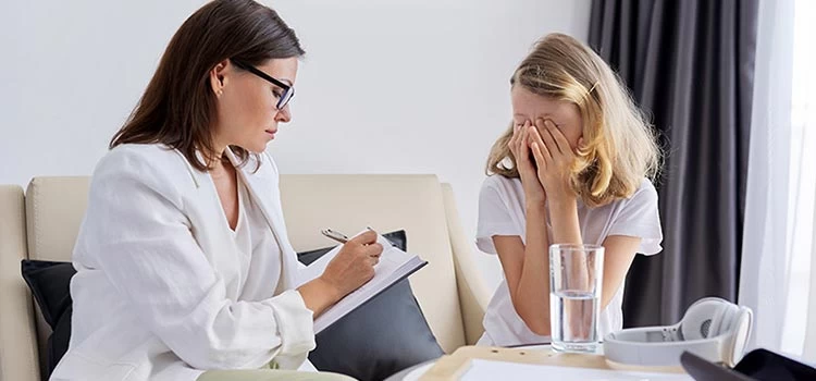 A female psychologist jotting down all the sad feelings on a notepad of a little girl at a therapy session.