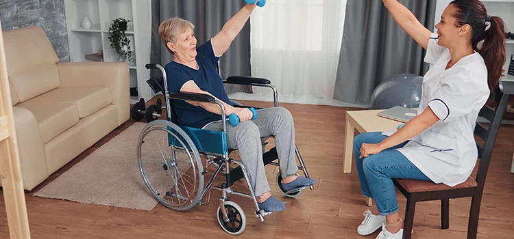 Female carer helping an elderly lady in a wheelchair with some exercises.