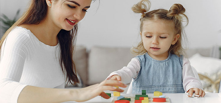 Female tutor assisting a little girl in assembling cubes.