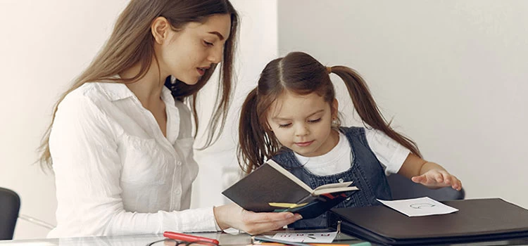 Tutor helping the little girl studying while showing something interesting on the notepad.