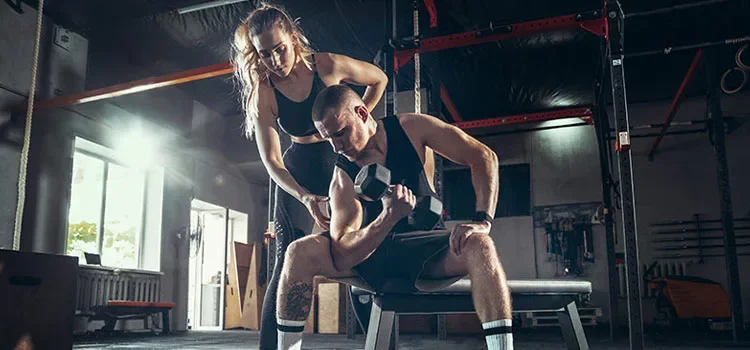 A female personal trainer showing the correct way of lifting dumbbells to a male trainee