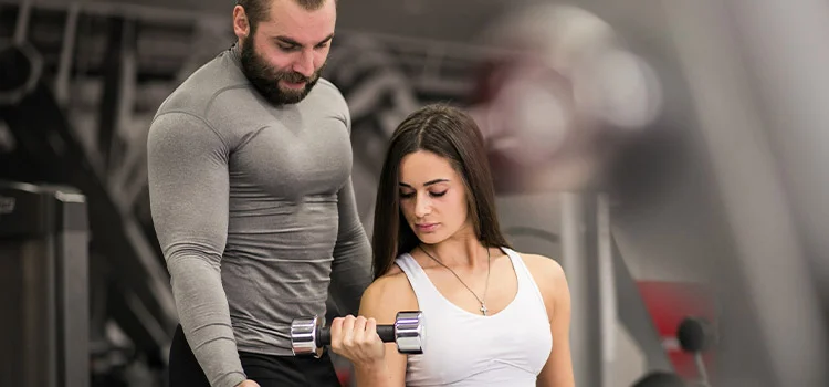 A male personal trainer helping a female trainee lift dumbbells 