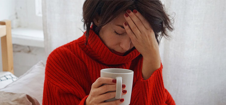 A woman holding a mug experiencing headache in the morning