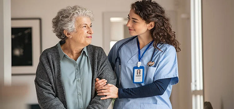 Female care worker helping a senior woman walking with a cane.