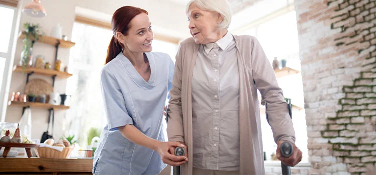 Female care worker helping a senior woman walking with crutches.