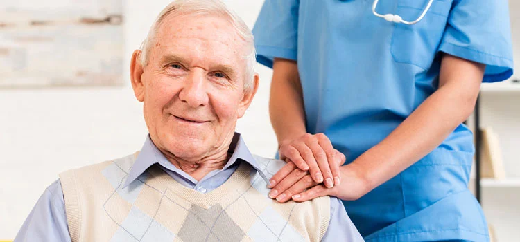Female carer placing her hands on the shoulder of a happy aged man.