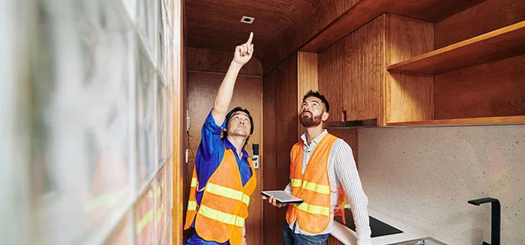 A Young Electrician in Orange Vest Shows Bulb Socket To Contractor On Ceiling