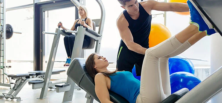 Young woman doing leg exercises in gym with the help of personal trainer.
