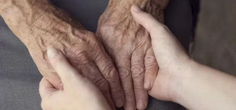 A young person holding the hands of an elderly with care