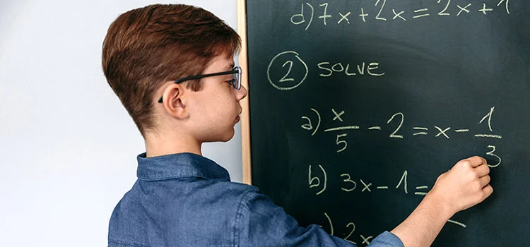 A young boy trying to solve maths problems on a blackboard