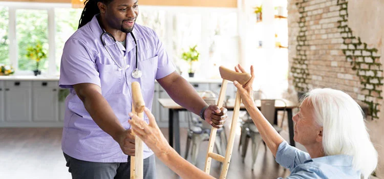 A nurse offering help to an elderly woman to stand up