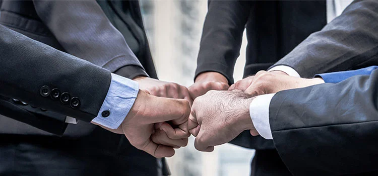 People in suits fisting bump their fists together to show power and unity in the office. 
