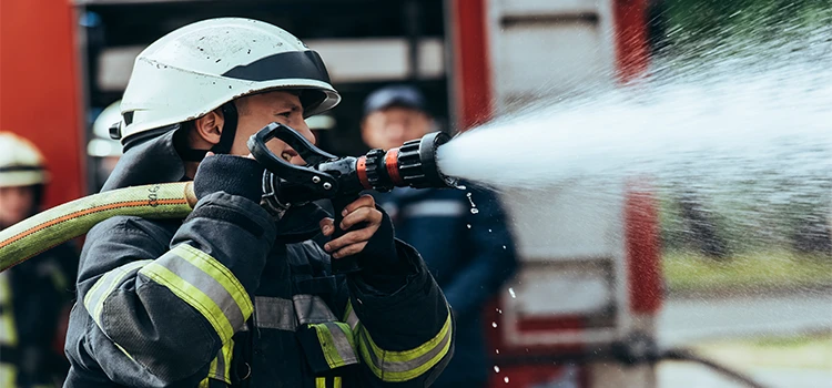 A firefighter with water hose extinguishing fire on street