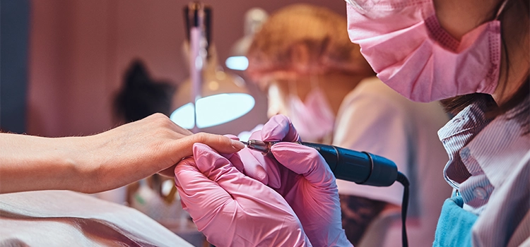 A young female nail master is working on client's cuticle in a nail salon. 