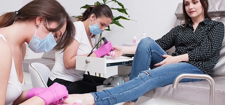 Two Nail Techs grooming their client's fingers and toenails. They are maintaining proper hygiene and ensuring clients's comfort. 