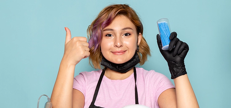 A nail artist showing thumbs up with a bunch of nail polishes and tools.