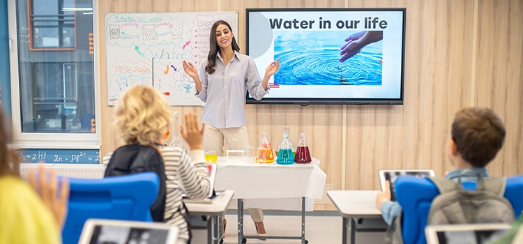 A high school teacher explaining a topic with a smart board & students have modern equipment as well. 