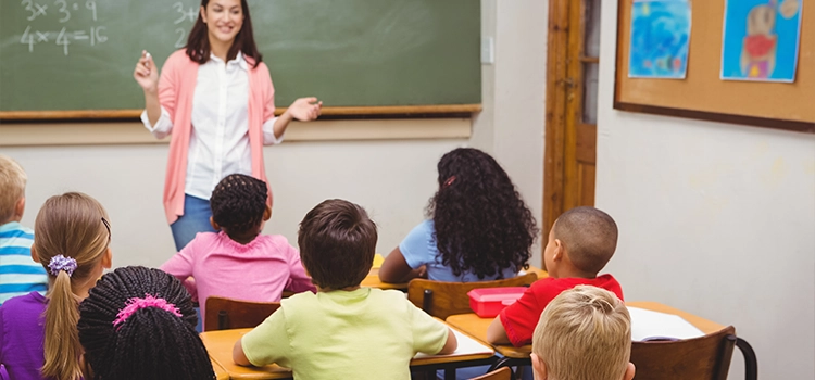 An elementary school teacher happily teaching students while writing on the board. 