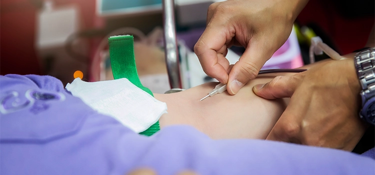 A phlebotomist inserting a cannula into a patient’s hand gently.