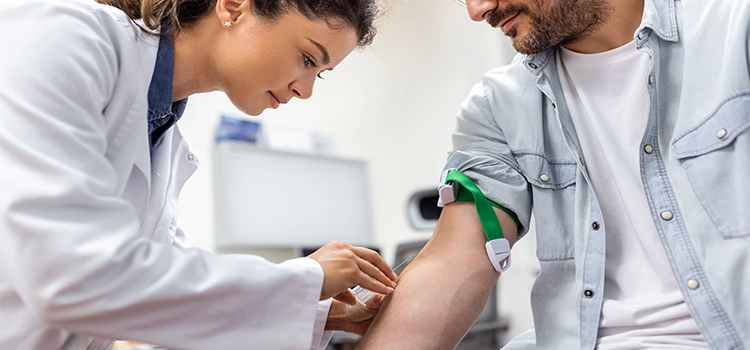 A phlebotomist drawing blood from a masked patient.