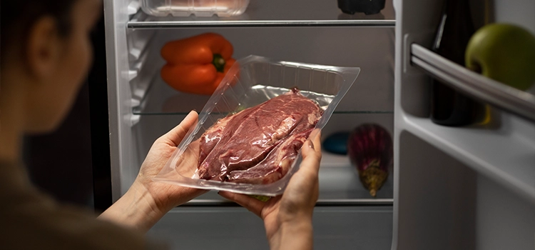 A woman placing a piece of lamb meat in the refrigerator for thawing. 